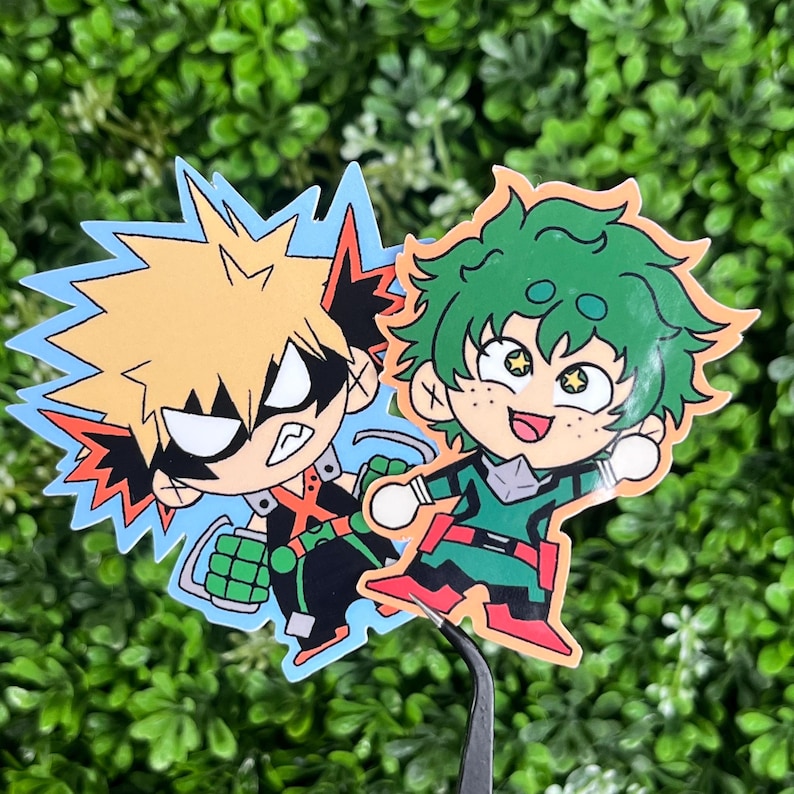 May include: Two cartoon stickers featuring anime characters. One has spiky blonde hair and a black outfit with green gloves, set against a blue background. The other has green hair and a green and red outfit. Both are smiling.