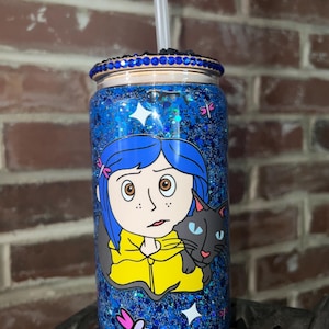 May include: A blue and black glitter tumbler with a blue rhinestone rim. The tumbler features a cartoon image of a girl with blue hair and a black cat. The girl is wearing a yellow jacket. The tumbler has a clear straw.