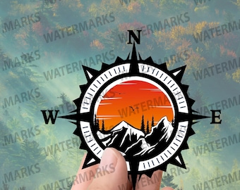 May include: Black compass design featuring a mountain and sunset scene. The compass has the letters N, W, E, and S, with a circular design and a mountain landscape inside. The background is a blurred forest.