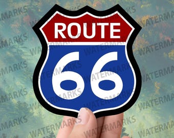 May include: A Route 66 sticker with a shield design. The top section is red, with white text reading "ROUTE". The bottom section is blue, with the number "66" in white. The sticker is held by a hand against a blurred forest background.