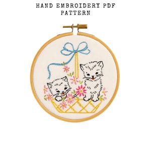 May include: Hand embroidery PDF pattern featuring two kittens in a basket with pink flowers. The design is set in a wooden embroidery hoop. The text "HAND EMBROIDERY PDF PATTERN" is at the top.