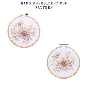Puede incluir: Dos aros de bordado con diseños florales. El bordado presenta hilo rosa y dorado sobre un fondo blanco. El texto "HAND EMBROIDERY PDF PATTERN" está en la parte superior. Los aros están sujetos en marcos de madera.