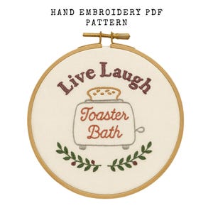 May include: Hand embroidery PDF pattern in a wooden hoop. The design features the words "Live Laugh" above a toaster with the words "Toaster Bath" below. Green and brown leaf accents are at the bottom. The text "HAND EMBROIDERY PDF PATTERN" is at the top.