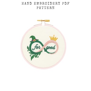 Könnte beinhalten: Handstickmuster-PDF mit einem Design mit einem grünen Hexenhut, einer goldenen Krone und den Worten "for good" in grüner Schrift. Das Design befindet sich in einem rosa Stickrahmen.