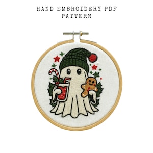 May include: Hand embroidery PDF pattern featuring a cartoon ghost wearing a green beanie and holding a drink and gingerbread man. The design is set in a wooden embroidery hoop. The text "HAND EMBROIDERY PDF PATTERN" is at the top.
