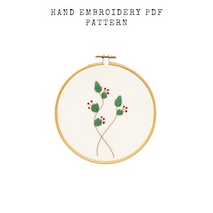 May include: A hand embroidery PDF pattern featuring a floral design. The embroidery is set in a wooden hoop and includes green leaves and red berries on brown stems. The text "HAND EMBROIDERY PDF PATTERN" is at the top.
