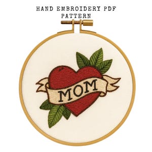 May include: Hand embroidery PDF pattern featuring a red heart with a banner that reads "MOM". The heart is surrounded by green leaves, all within a wooden embroidery hoop. The text "HAND EMBROIDERY PDF PATTERN" is at the top.