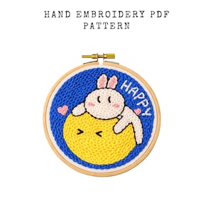 May include: Hand embroidery PDF pattern. The design features a white bunny and yellow chick on a blue background, with the word "HAPPY". The embroidery is set in a wooden hoop. The text "HAND EMBROIDERY PDF PATTERN" is at the top.