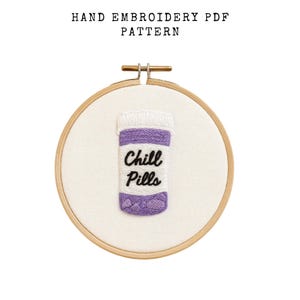 Puede incluir: Patrón PDF de bordado a mano con un diseño de botella de pastillas morada y blanca con las palabras "Chill Pills" bordadas en negro. El diseño está en un bastidor de bordado de madera.