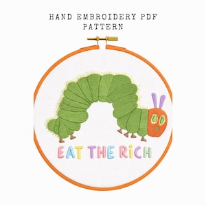 May include: Hand embroidery PDF pattern featuring a green caterpillar with an orange head and purple antennae. The caterpillar is embroidered on white fabric within an orange embroidery hoop. The text "EAT THE RICH" is embroidered below the caterpillar.