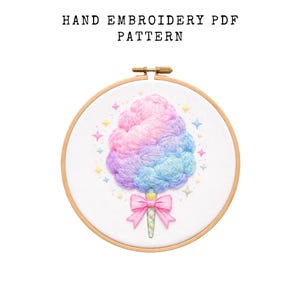 May include: Hand embroidery PDF pattern featuring a colorful cotton candy design. The cotton candy is rendered in shades of pink, purple, and blue, with a pink bow and star accents. The design is set within a wooden embroidery hoop.