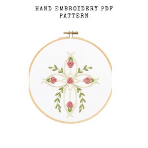 May include: A hand embroidery PDF pattern featuring a floral design. The design is centered on a white fabric stretched within a wooden embroidery hoop. The floral pattern includes pink roses and green leaves. The text "HAND EMBROIDERY PDF PATTERN" is at the top.