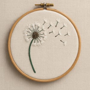 May include: Embroidered dandelion art in a wooden hoop. The dandelion is white with a brown center and a green stem. Several white seeds are blowing away from the flower. The background is a light beige fabric.