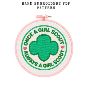May include: A hand embroidery PDF pattern with a Girl Scout theme. The design features a green trefoil, the words "Once a Girl Scout, Always a Girl Scout," and pink hearts, set within a pink embroidery hoop.