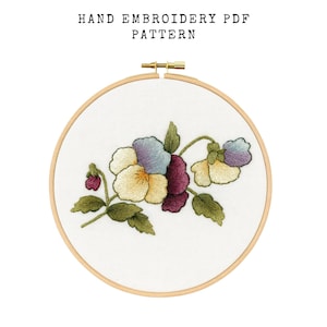 May include: Hand embroidery PDF pattern featuring a floral design. The embroidery is set in a wooden hoop and showcases a cluster of flowers in shades of yellow, purple, and blue, with green leaves. The text "HAND EMBROIDERY PDF PATTERN" is at the top.