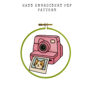 May include: Hand embroidery PDF pattern featuring a pink camera with a photo of a cat, set within a green embroidery hoop. The text "HAND EMBROIDERY PDF PATTERN" is at the top.