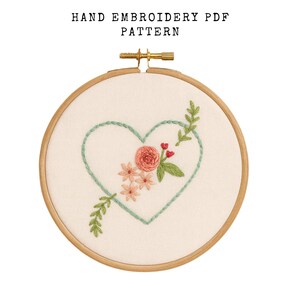 May include: A hand embroidery PDF pattern featuring a heart design with floral accents. The design includes a light green heart outline, a pink rose, small pink flowers, and green leaves. The text "HAND EMBROIDERY PDF PATTERN" is at the top.