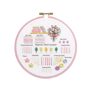 May include: A Beginner Stitch Sampler embroidery hoop with a pink frame. The white fabric displays various stitch examples, including Split Stitch, Back Stitch, and French Knot Stitch. A bouquet of pink flowers is also shown.