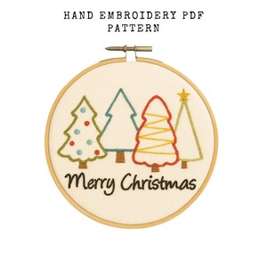 May include: Hand embroidery PDF pattern featuring a festive design. The artwork includes four embroidered Christmas trees in green, blue, and red, with a yellow star. The words "Merry Christmas" are stitched below the trees, all within a wooden embroidery hoop.