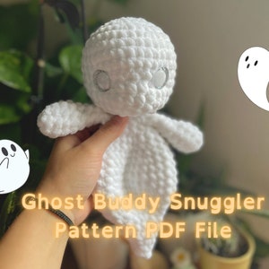 May include: White crocheted ghost amigurumi toy with sparkly eyes. The toy is being held by a hand and the text "Ghost Buddy Snuggler Pattern PDF File" is in the foreground.