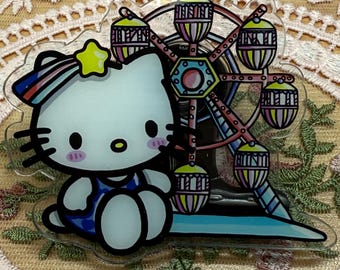 May include: A clear acrylic charm featuring a cartoon cat character with a rainbow bow and a yellow star. The cat sits next to a colourful Ferris wheel with gondolas. The charm has a clear border.