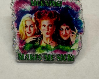 May include: A glittery pin featuring three women with the text "OH WHAT A GLORIOUS MORNING! MAKES ME SICK!". The women have blonde, red, and black hair, set against a colourful background.