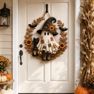 May include: A circular autumn wreath featuring a central ghost figure wearing a black witch hat with sunflowers, patches, and boots. The wreath is decorated with orange leaves, berries, sunflowers, two black bats, and a black cat holding a lantern.
