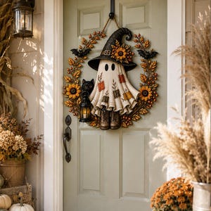 May include: A circular wreath featuring a central ghost figure wearing a black witch hat with sunflowers, brown boots, and a patchwork fabric body. The wreath is decorated with autumn leaves, sunflowers, and two black bats, with a black lantern.