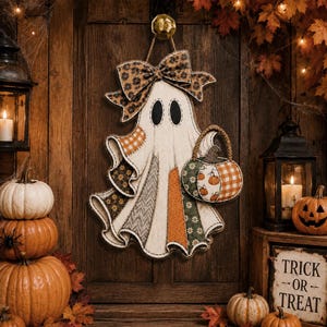 Puede incluir: Una decoración de pared de fantasma colgante con un diseño de patchwork que incluye varios patrones de tela como cuadros naranjas, flores y estampados de espiga. El fantasma sostiene una pequeña cesta de calabaza y un lazo grande.