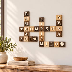 May include: A wall-mounted crossword puzzle display made of dark and light wood tiles. The tiles feature letters and numbers, forming the names Emma, Thompson, Zoe, Liam, Ava, and Milo, along with a heart symbol and a paw print icon.