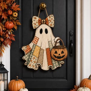 May include: A hanging ghost decoration featuring a patchwork-style body with various orange, green, and cream fabric patterns. The ghost has a large bow at the top and holds a brown jack-o'-lantern bucket with a carved face and a braided handle.