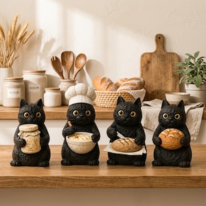 May include: Four black cat figurines with textured surfaces and large yellow eyes. One cat wears a white chef hat and holds a mixing bowl, while the others hold a small jar, a loaf of bread on a white cloth, and a round loaf of bread respectively.