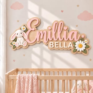 May include: A wall-mounted name sign featuring the name Emillia Bella in pink and white script and block lettering. The sign is decorated with a white rabbit figure, green leaves, and white daisy flowers with yellow centers on a tan base.