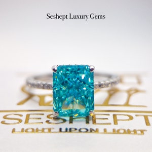 May include: A turquoise square-shaped gemstone ring with a silver band. The ring is set on a white surface with the text "Seshept Luxury Gems" above it.