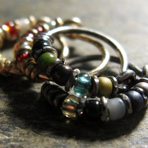 May include: Three silver hoop earrings with colourful beads. The beads are green, blue, yellow, red and black.