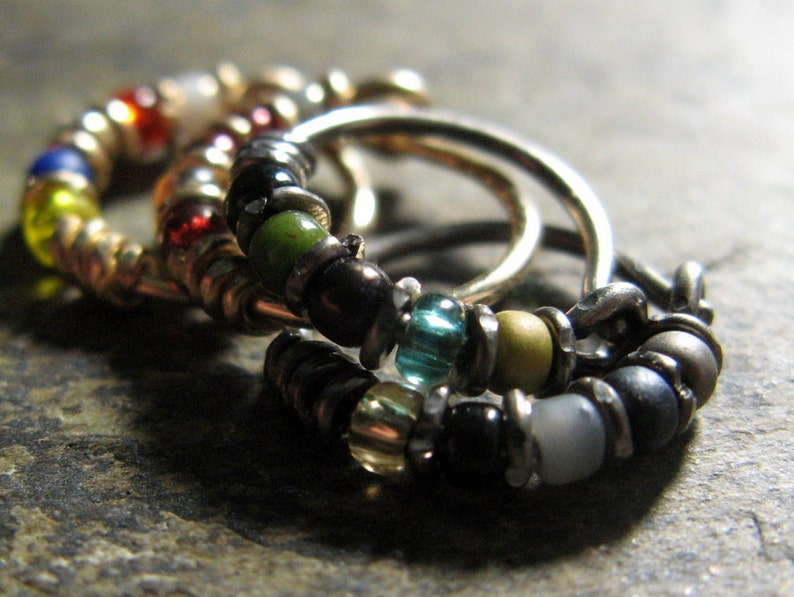 May include: Three silver hoop earrings with colourful beads. The beads are green, blue, yellow, red and black.