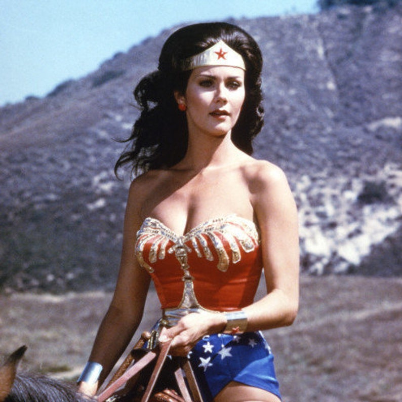 May include: A woman wearing a red, white and gold bustier with a star-shaped headband. She is holding a whip and wearing a blue and white skirt.