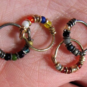 May include: Three small hoop earrings with colourful beads. The hoops are made of silver and gold metal. The beads are red, white, blue, green, black and yellow.