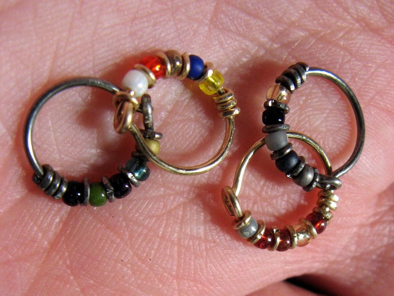 May include: Three small hoop earrings with colourful beads. The hoops are made of silver and gold metal. The beads are red, white, blue, green, black and yellow.