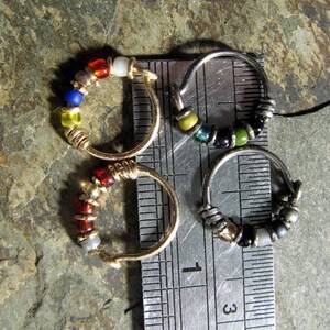 May include: Three silver hoop earrings with colourful glass beads. The hoops are lined up on a ruler with the numbers 1 and 3 visible.