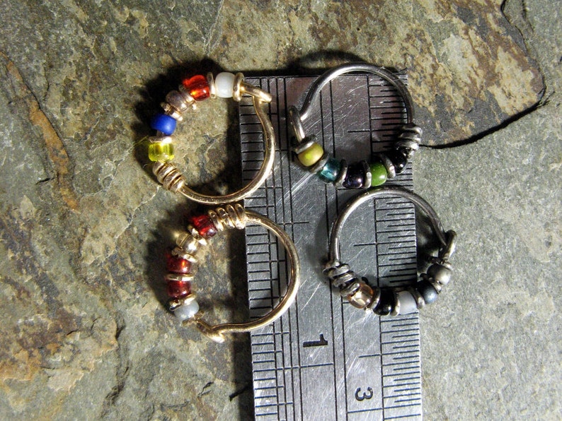 May include: Three silver hoop earrings with colourful glass beads. The hoops are lined up on a ruler with the numbers 1 and 3 visible.