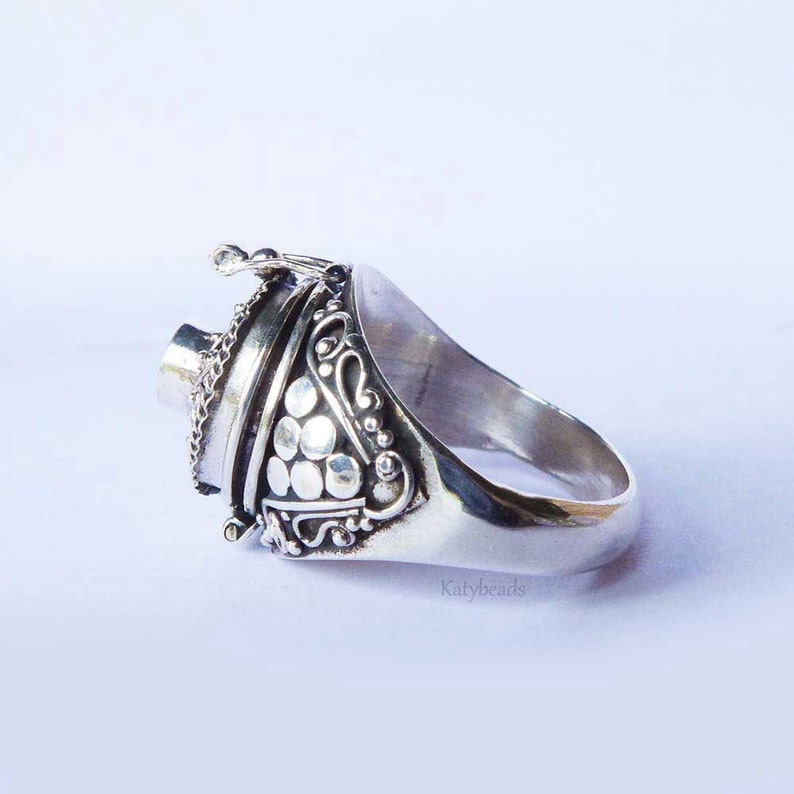 Puede incluir: Un anillo de plata con detalles ornamentados y un compartimento con bisagras. El anillo presenta una cadena decorativa y una serie de peque&ntilde;as decoraciones circulares. El anillo es probablemente de plata de ley.