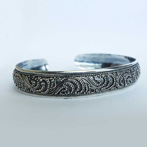 Puede incluir: Brazalete de plata con intrincados detalles de volutas y patrones de puntos. El diseño abierto presenta una banda texturizada con un motivo floral repetitivo. Una pieza de joyería clásica.
