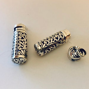 May include: Three silver-colored, cylindrical pendants with intricate, openwork scroll designs. One pendant is open, revealing the interior. The pendants are on a white surface. The design is consistent across all pieces.