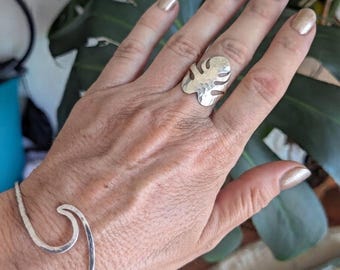 May include: A silver-toned metal ring featuring a cutout monstera leaf design with a hammered texture, paired with a matching silver-toned metal cuff bracelet shaped like a stylized ocean wave with a consistent hammered finish throughout.