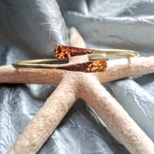 May include: A gold hammered metal bracelet with a unique open design. The bracelet is made of a single piece of metal that is bent into a circle and then hammered to create a textured surface.