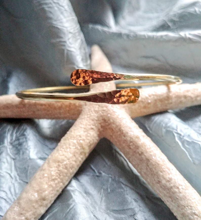 May include: A gold hammered metal bracelet with a unique open design. The bracelet is made of a single piece of metal that is bent into a circle and then hammered to create a textured surface.