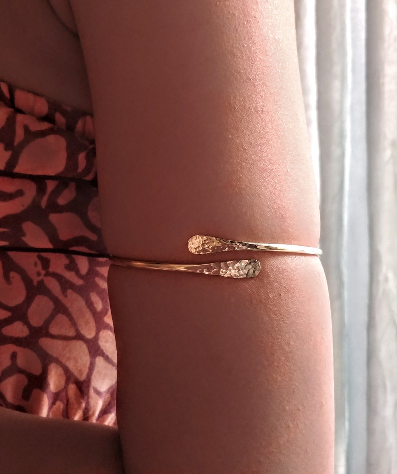 May include: A gold hammered metal arm cuff bracelet. The bracelet is open and has a simple design.