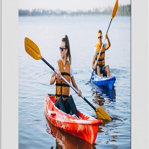 May include: Two people kayaking on a lake. The person in the foreground is in a red kayak, wearing a life vest and sunglasses, and holding a yellow paddle. The other person is in a blue kayak, also wearing a life vest and holding a paddle.