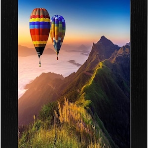 May include: Two colourful hot air balloons float above a mountain range with a misty valley below. The sky is a vibrant blue with a pink and orange sunset in the background.